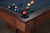The Jackie's Pool Table in Pecan Bourbon Walnut boasts luxurious leather pockets, stainless steel 'Made in the USA' logo, and premium billiard felt. Fully customizable and crafted in the USA, exclusively at Sawyer Twain.