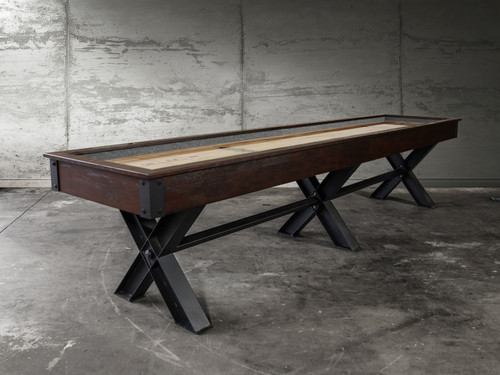 Portland Shuffleboard Table - Full View: A stunning modern industrial shuffleboard table featuring a distressed wood cradle and bold X-leg metal base, shown in a contemporary game room setting.